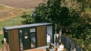 Zona relax esterna moderna con una panca di legno e un tavolino, circondata da un recinto in metallo e un albero.