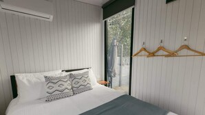 Una camera da letto con un letto, due cuscini decorati, una coperta grigia e appendini in legno sulla parete.