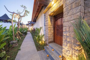 A pathway leading to a stone building with a wooden door and steps adorned with orange flowers. - Dewi Kunti Villa (Sebatu)