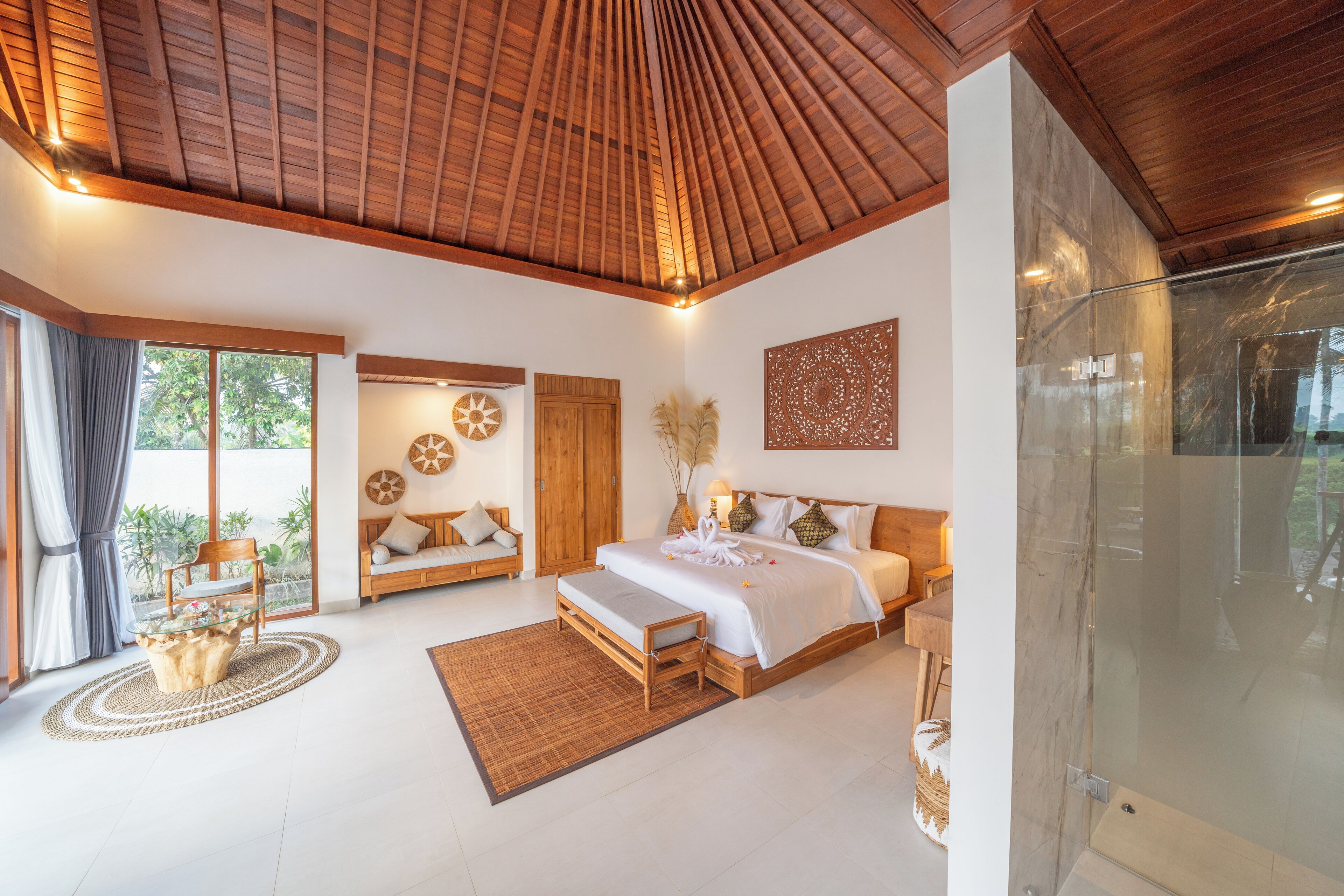 A spacious bedroom with a large bed, a glass shower, and a view of the outdoors.