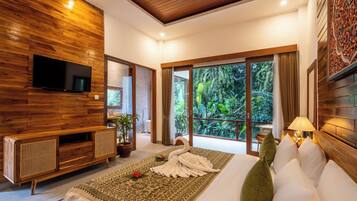 Un dormitorio moderno con pared de madera, televisor de pantalla plana, sofá, cama con cabecera decorativa y vista a follaje exuberante a través de grandes ventanales.