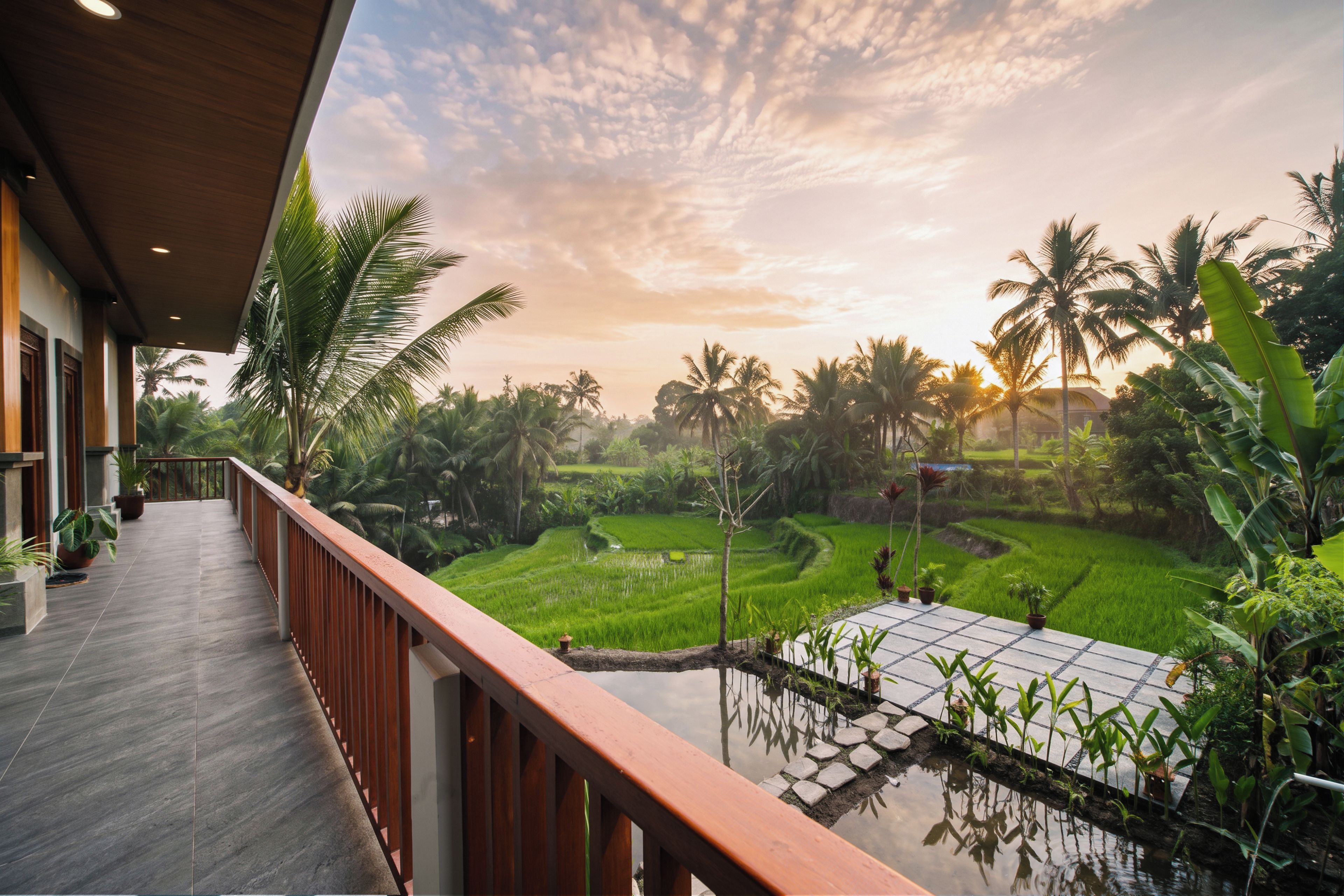 Uma varanda com vista para um jardim exuberante e um campo de arroz.