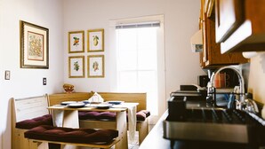 Una pequeña cocina con comedor, una ventana y cuadros en la pared.