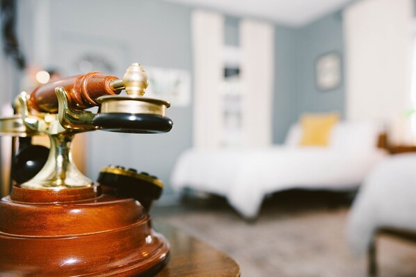 A vintage rotary phone on a wooden table in a hotel room with a bed and a nightstand in the background.