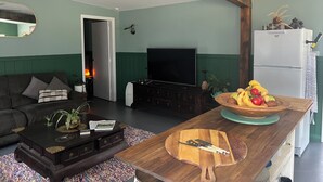 A living room with a dark brown sofa, a wooden coffee table, a TV, and a refrigerator. - The Australian Farm Retreat (Stockinbingal)