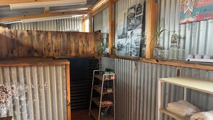 A compact, rustic bathroom with wooden beams, a corrugated metal wall, and a shelf with towels and toiletries. - The Australian Farm Retreat (Stockinbingal)
