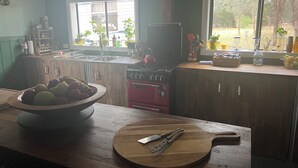A kitchen with a wooden countertop, a red stove, and a window with plants. - The Australian Farm Retreat (Stockinbingal)