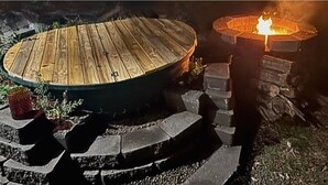 A circular wooden deck with a fire pit in the center, surrounded by stone steps and potted plants. - The Australian Farm Retreat (Stockinbingal)