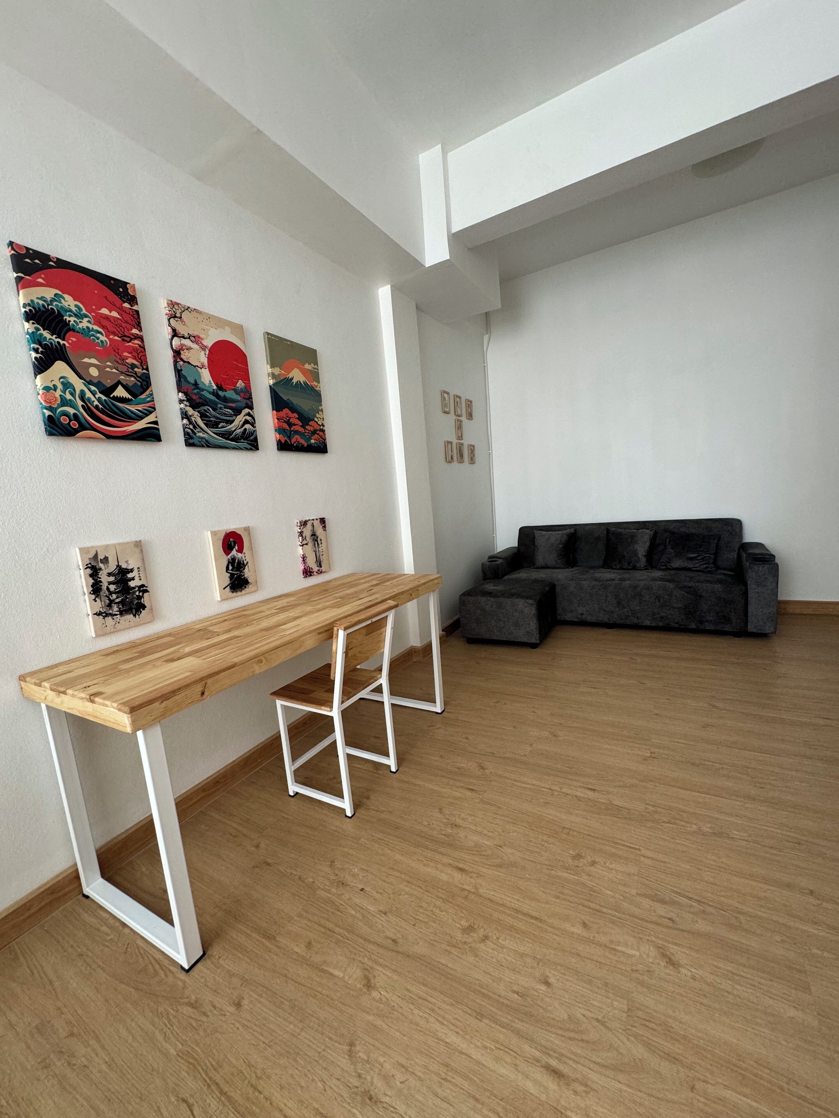A spacious room with a wooden floor, a dark grey sofa, and a wooden table with white legs.
