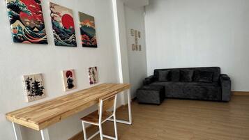 A spacious room with a wooden floor, a dark grey sofa, and a wooden table with white legs.