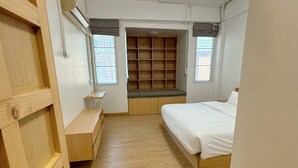 Une chambre à coucher de taille réduite, avec un lit en bois, des étagères intégrées et un petit coin salon.
