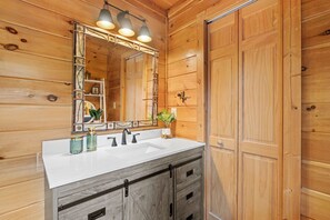 A wooden cabin bathroom with a white sink, dark wooden cabinets, and a large mirror with decorative elements.