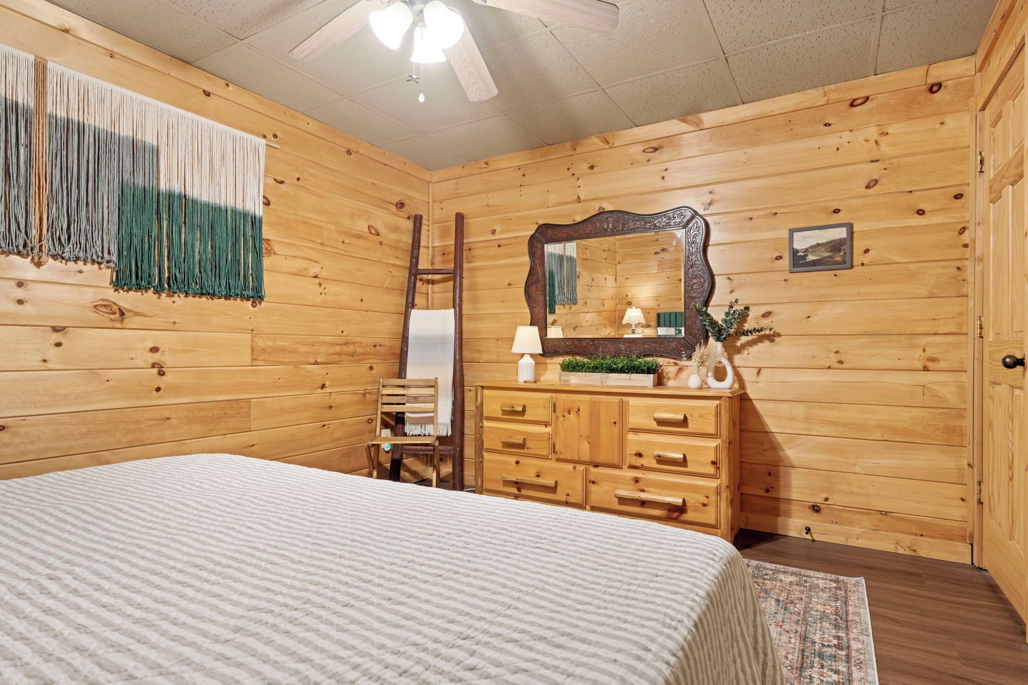 A wooden-paneled bedroom with a bed, dresser, mirror, and a ladder.