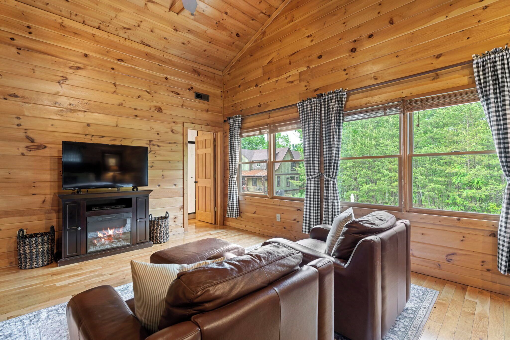 Ein gemütliches Blockhaus-Interieur mit Holzwänden, Kamin, Ledersofas und großen Fenstern mit Vorhängen.