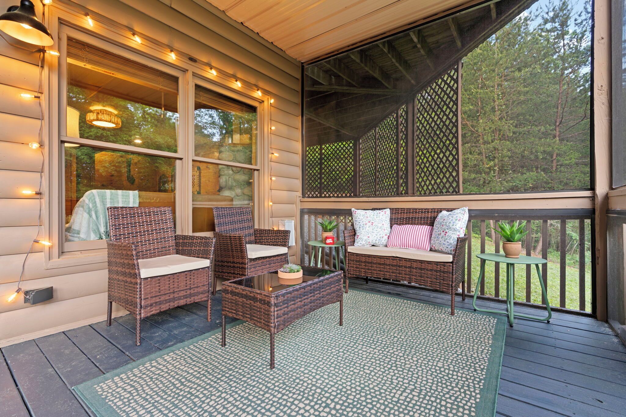 A covered porch with wicker furniture, a glass table, and a view of the surrounding forest.
