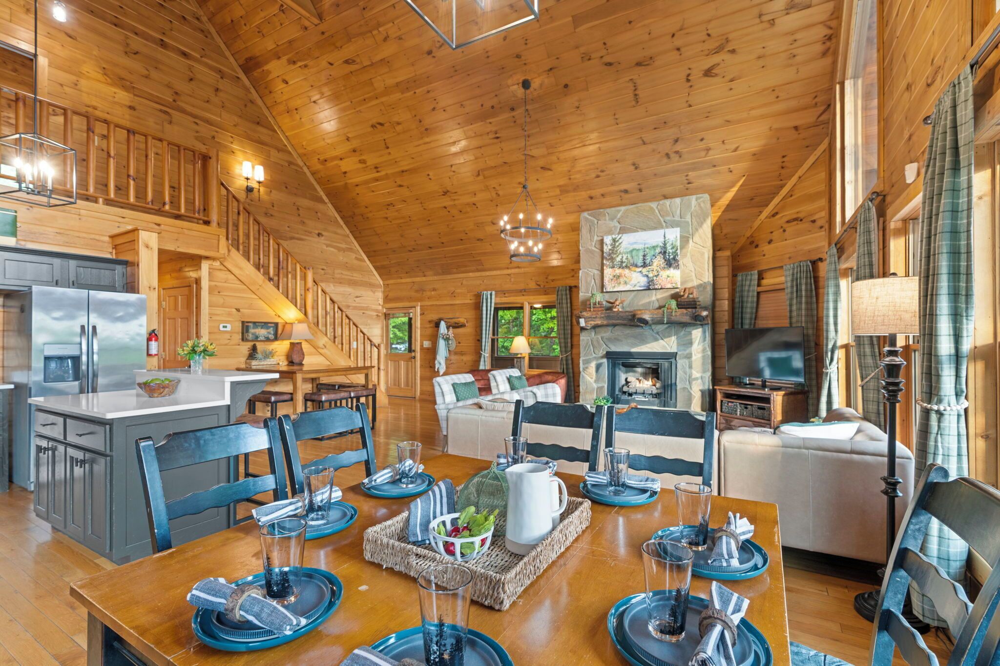 A spacious cabin with a wooden interior, a dining area with blue tableware, a fireplace, and a kitchen with modern appliances.