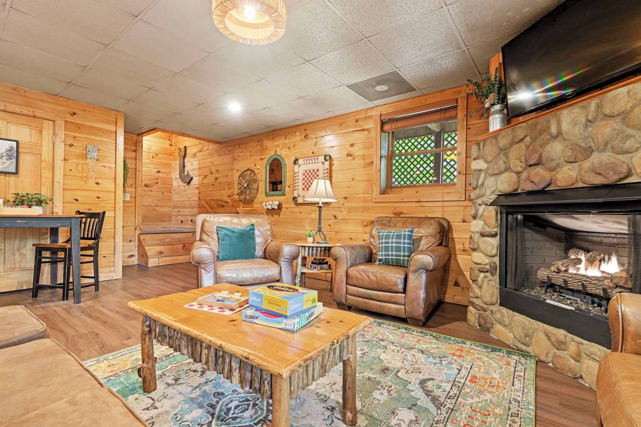 Un accogliente interno di una baita con camino in pietra, divani in pelle, un tavolino in legno e un televisore montato sopra il camino.