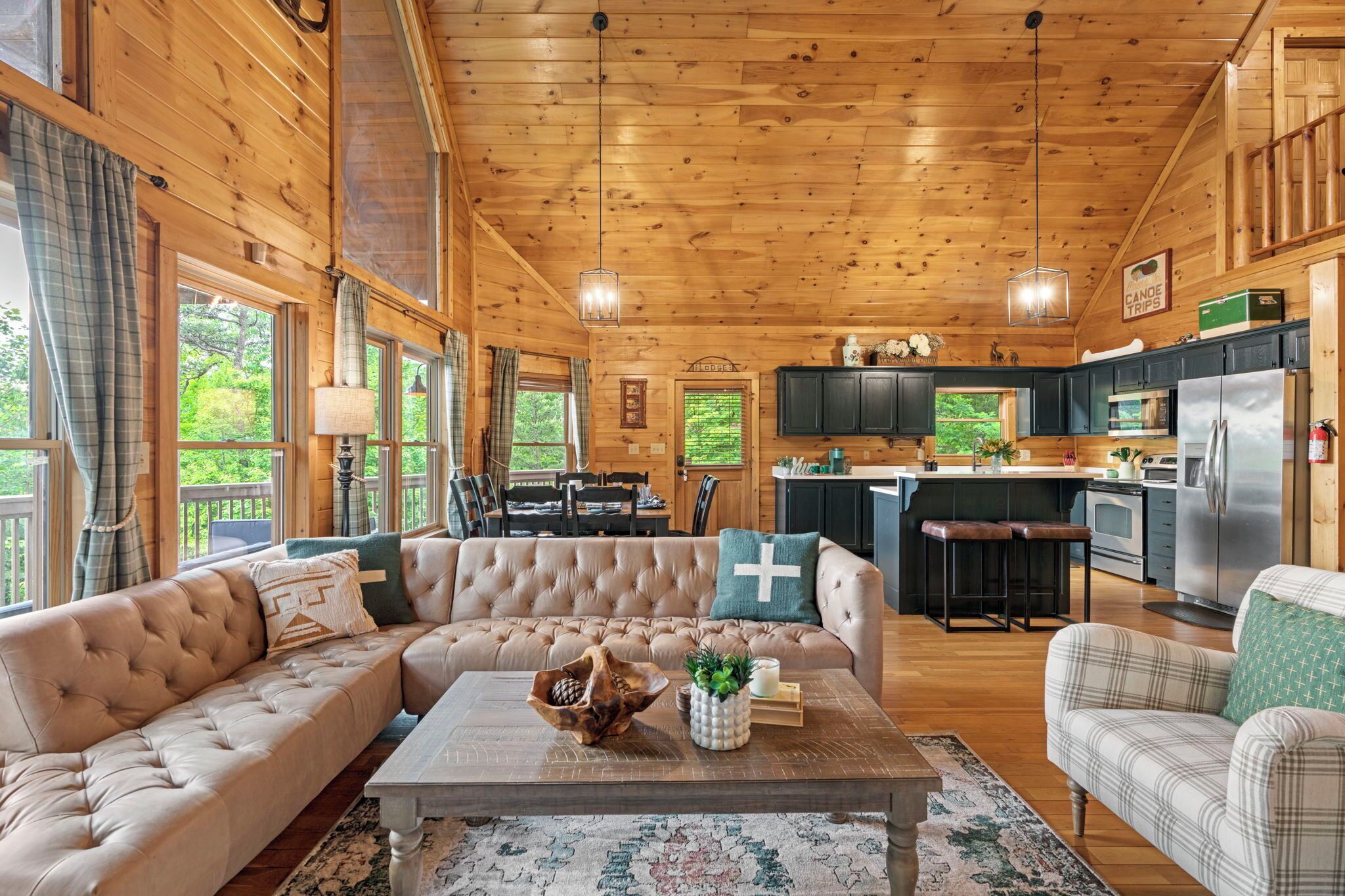 A spacious living room with a large beige sofa, a coffee table, and a view of the kitchen and dining area through large windows.