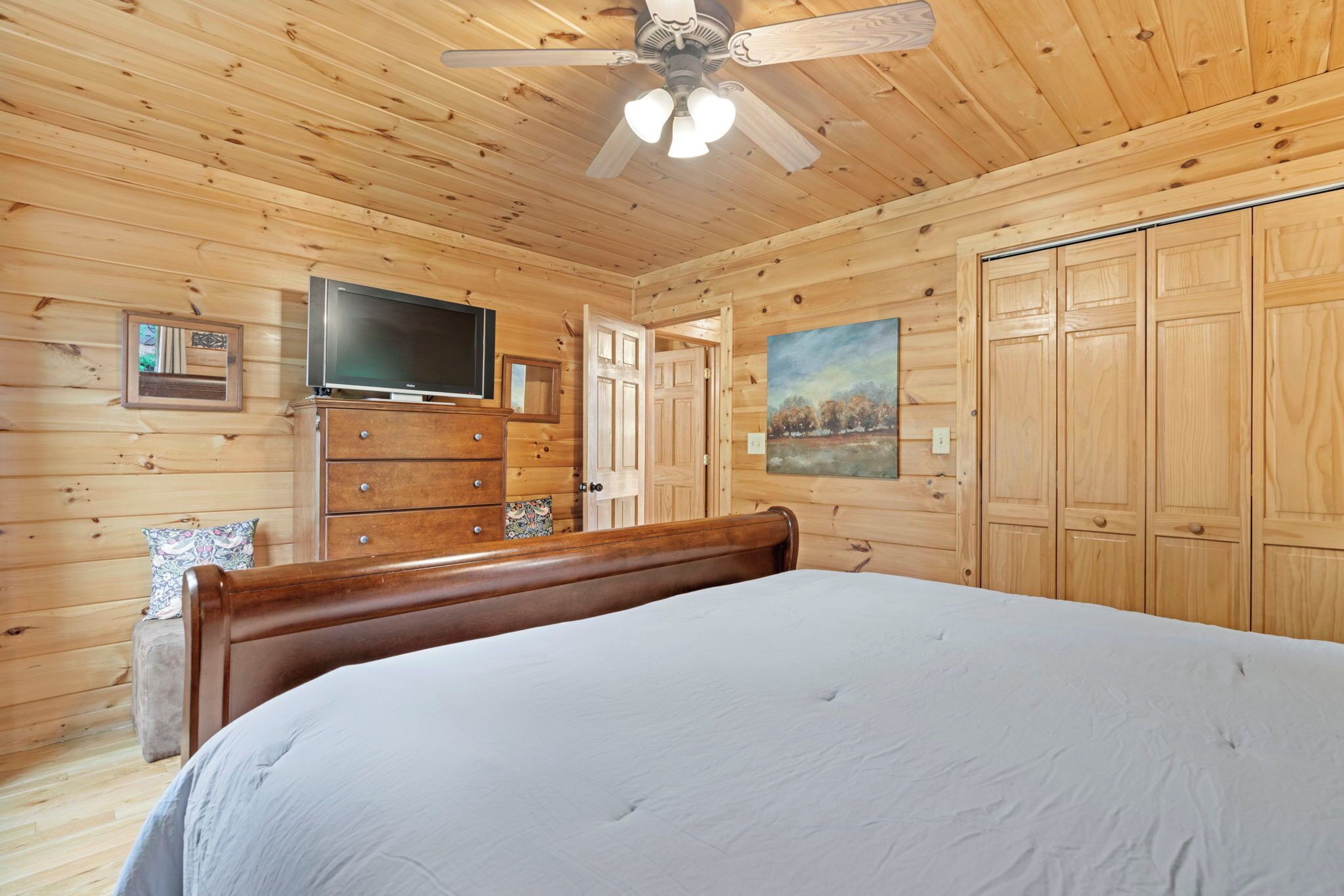 Une chambre dans une cabane en bois, avec un lit, une commode, une télévision et un tableau accroché au mur.