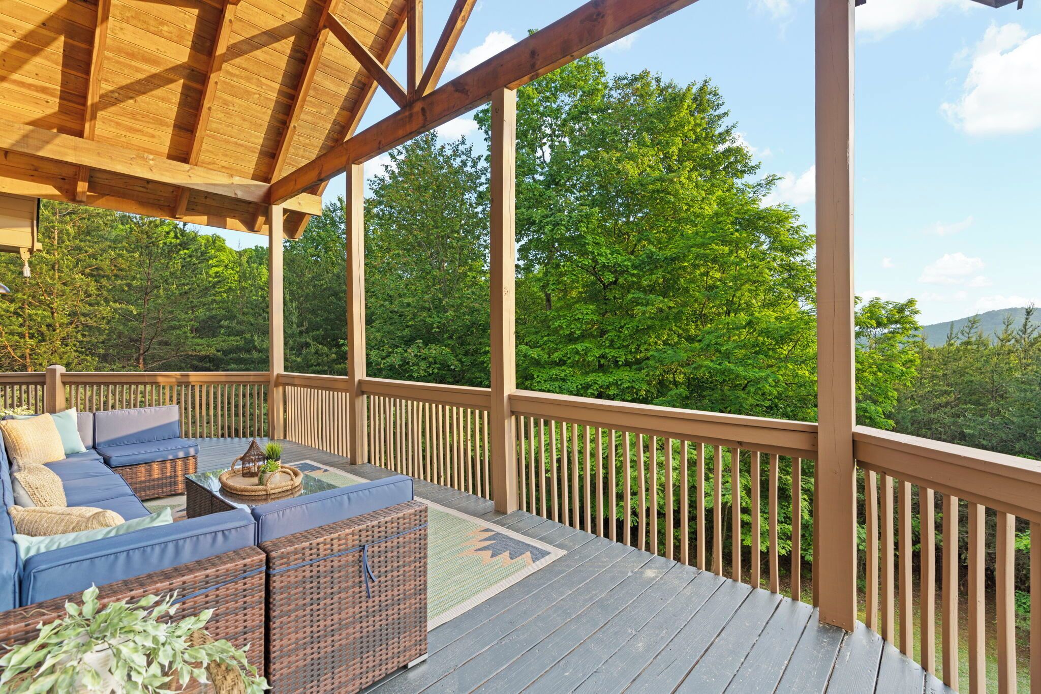 En overdækket terrasse med udendørs møbler, et pergola og udsigt til et skovområde.