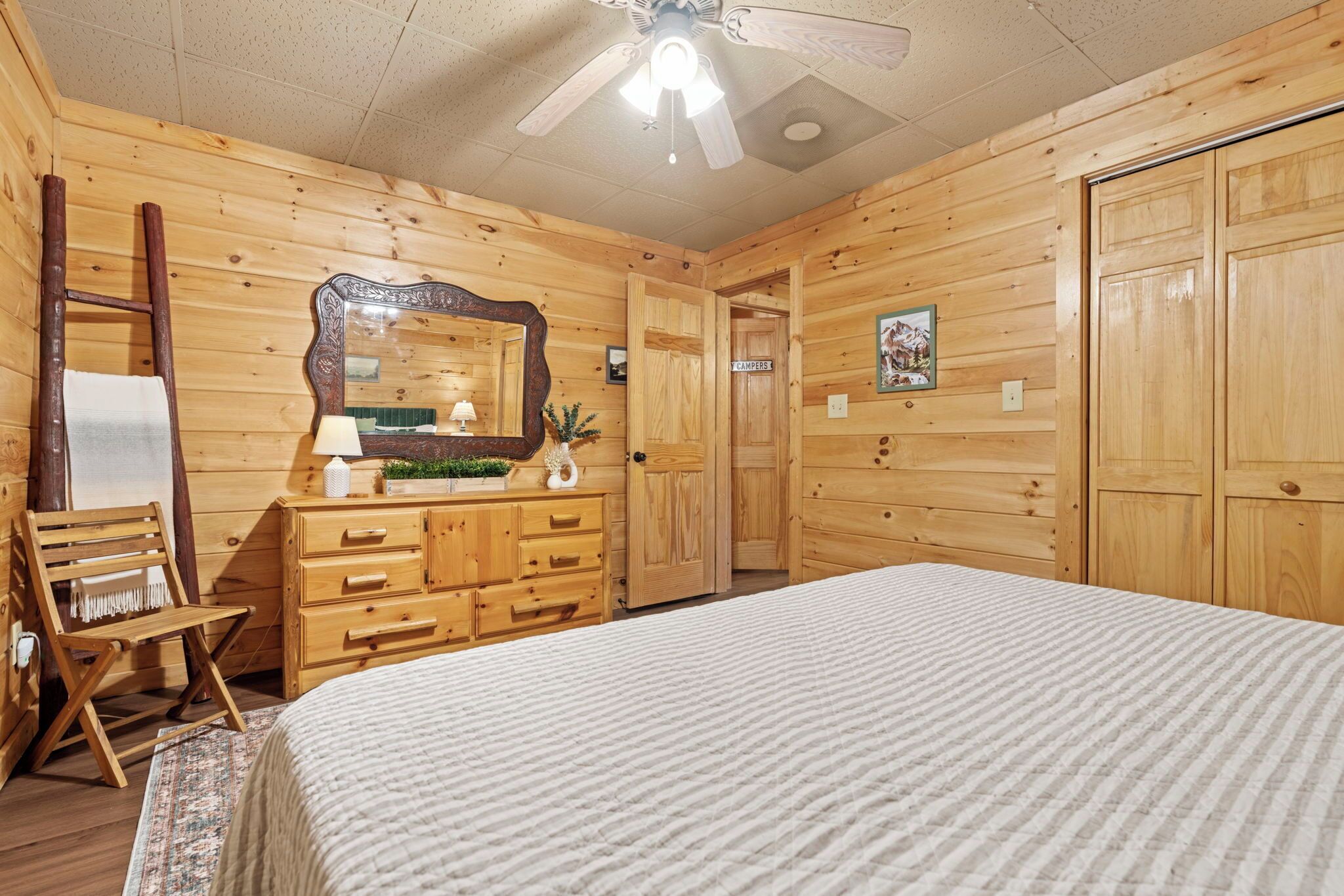 A wooden cabin room with a bed, dresser, mirror, and a door labeled "CAMPERS".
