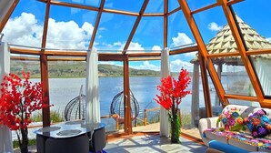 A spacious room with a large glass ceiling, a round table, and a sofa with colorful floral decorations. - Titicaca Glampina (Puno)