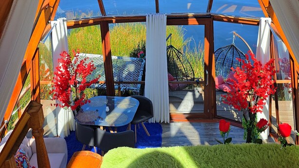 A cozy room with a large skylight, a wooden ceiling, and a view of a lake and hills. - Titicaca Glampina (Puno)