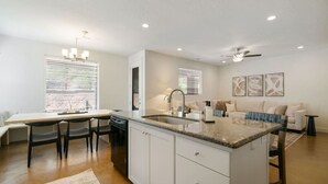 A modern kitchen with a central island, white cabinetry, and a dining area with a table and chairs. - Zion view~Hot Tub~Fire Pit~Sauna~Stargazing (Apple Valley)