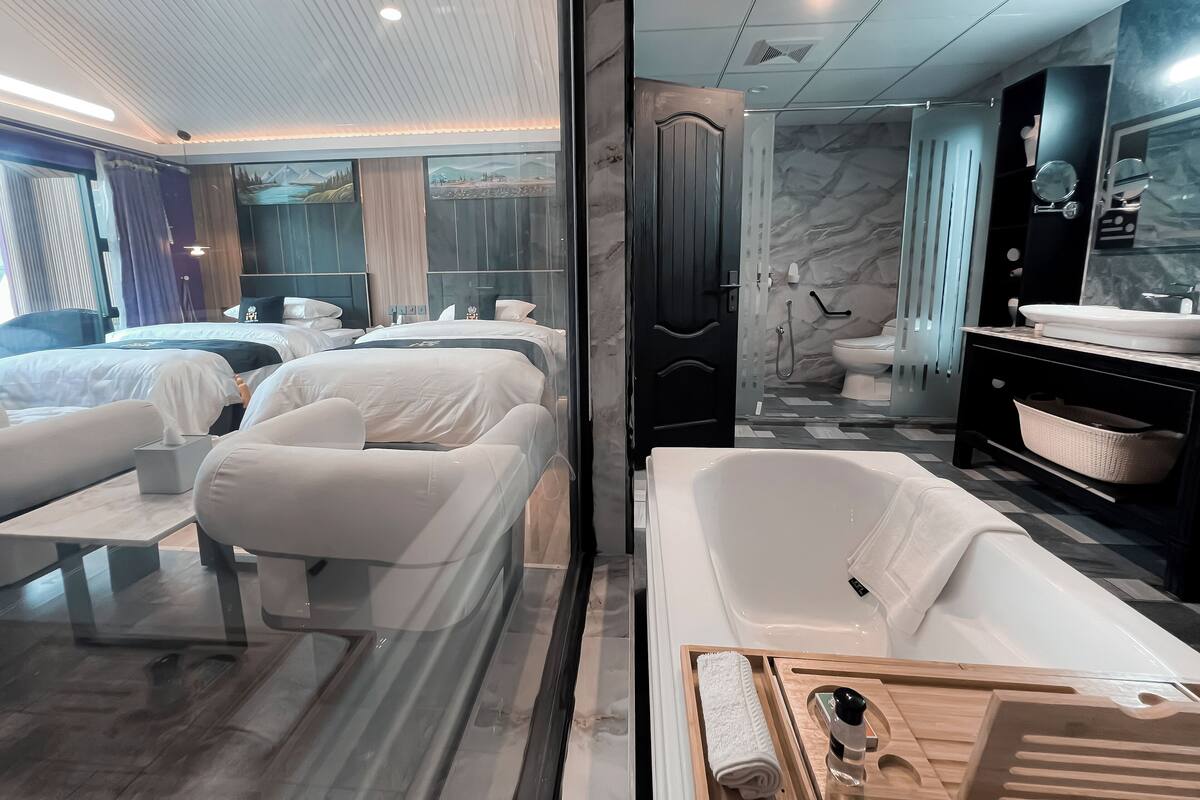 Une chambre d’hôtel moderne dotée d’un grand lit, d’un canapé séparé, d’une douche à l’italienne avec des parois en verre, et d’une salle de bain séparée avec une baignoire et un meuble-lavabo.