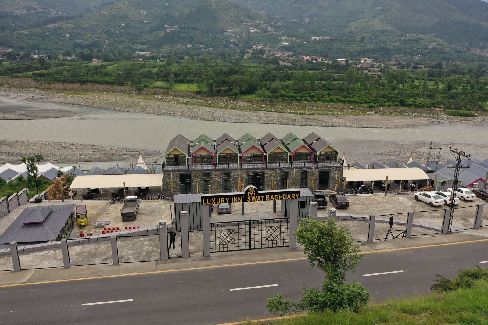Un hôtel avec une enseigne indiquant « LUXURY INN SWAT BAGHDARY » et une vue sur une rivière en arrière-plan.
