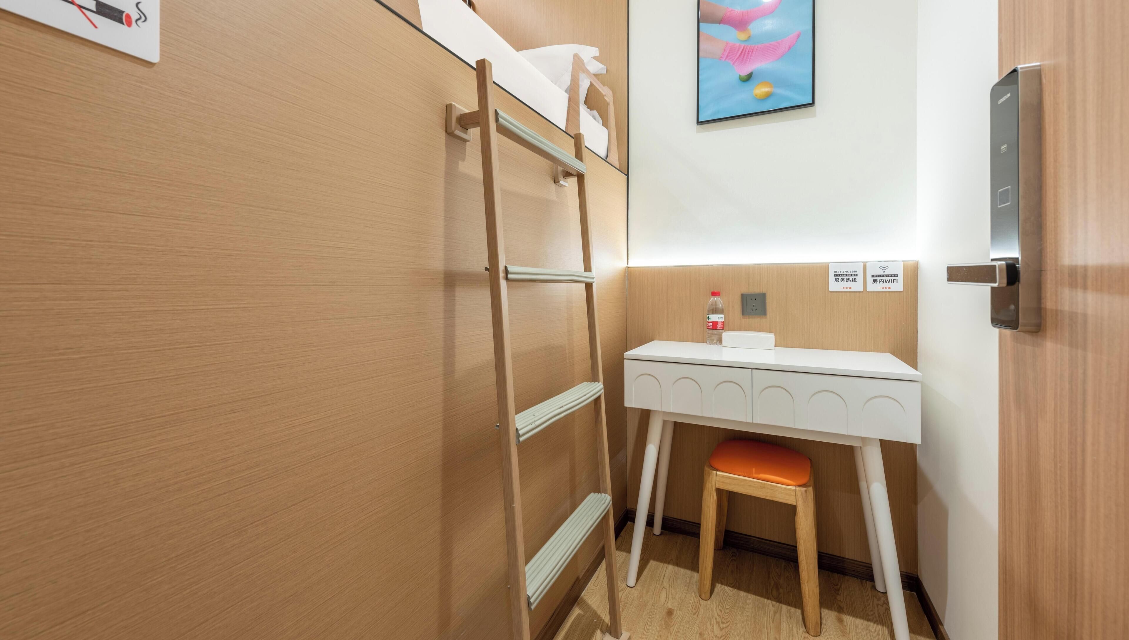 Une chambre d’hôtel compacte équipée d’un lit superposé, d’un petit bureau, d’une chaise et d’un téléviseur fixé au mur.
