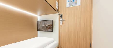 Een hotelkamer met een houten vloer, een wit bed, een aan de muur bevestigde televisie en een deur met een kaart en een bordje.