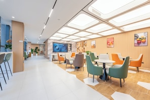 Un intérieur moderne avec un vaste espace d’accueil, des sièges disposés autour de tables et un grand écran affichant des informations.
