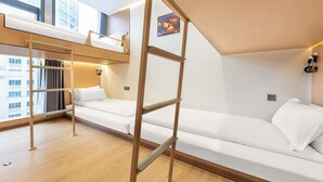 Una habitación de hotel moderna con una cama litera, una escalera de madera, un sofá y vistas a la ciudad.