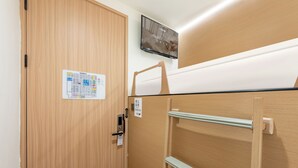 Habitación de hotel con puerta de madera, televisor montado y cama con cabecera de madera.