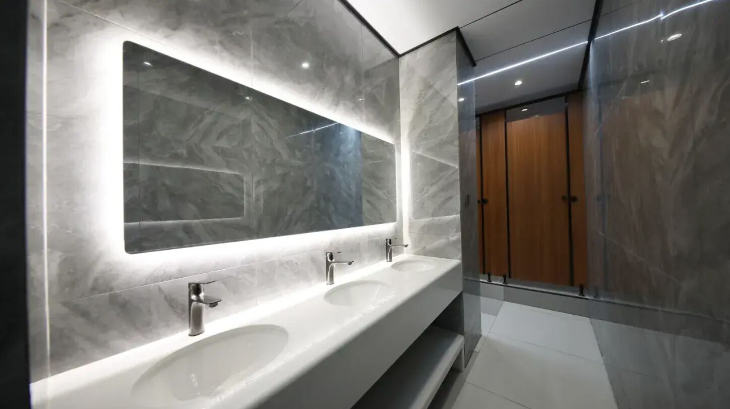 Un baño moderno con tres lavamanos, un espejo grande y una puerta de madera.