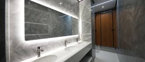 Un baño moderno con tres lavamanos, un espejo grande y una puerta de madera.