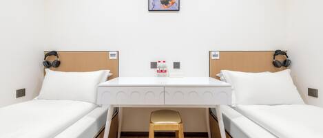 A hotel room with two single beds, a small table, a chair, and a painting on the wall.