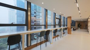 Un intérieur moderne avec de grandes fenêtres, un long comptoir avec des tabourets et un espace salon avec des tables et des chaises.