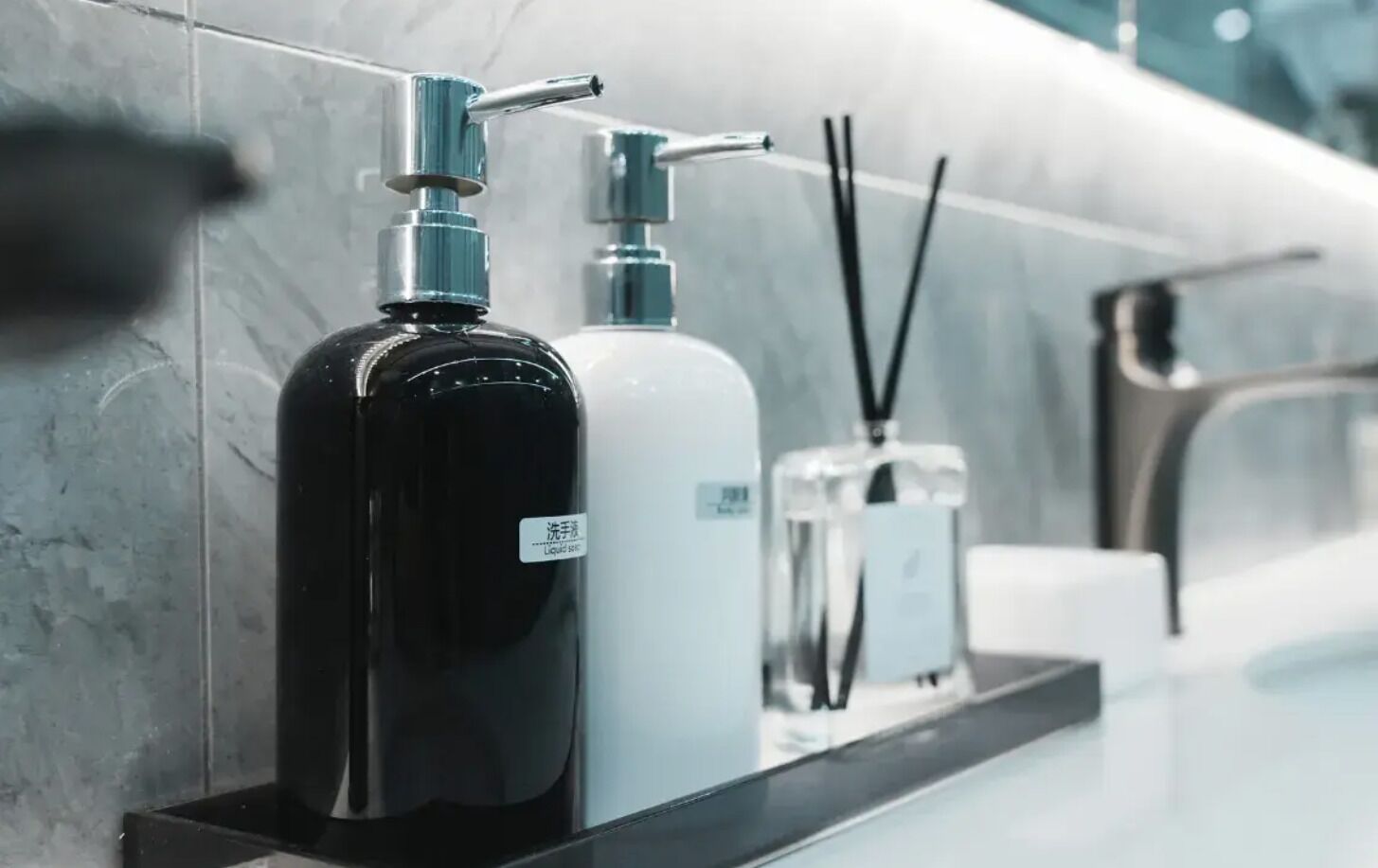 A bathroom with a marble wall, a black bottle, a white bottle, and a small container on a shelf.