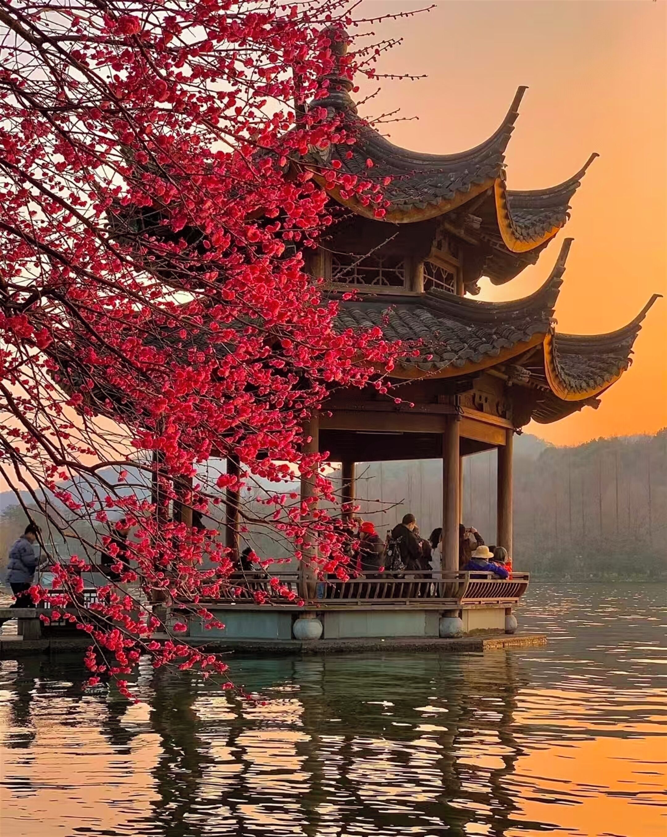 A traditional pavilion with a tiered roof structure, situated on a body of water, surrounded by a natural landscape.