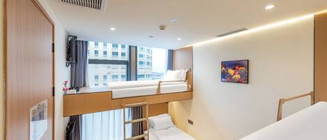 A compact hotel room with a bunk bed, a small desk, a window with curtains, and a painting on the wall.