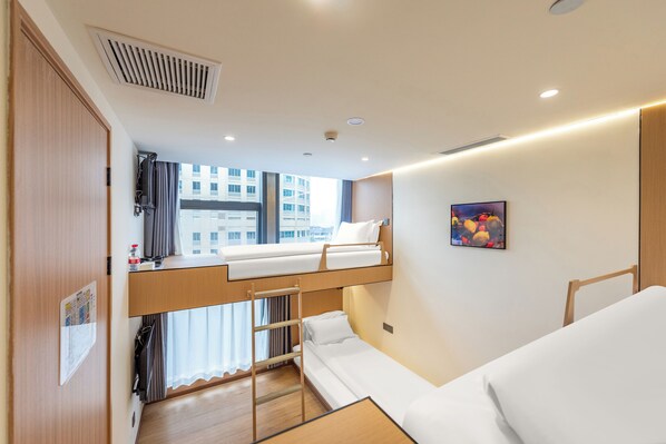 Ein kleines Hotelzimmer mit Etagenbett, einem kleinen Schreibtisch, einem Fenster mit Vorhängen und einem Bild an der Wand.