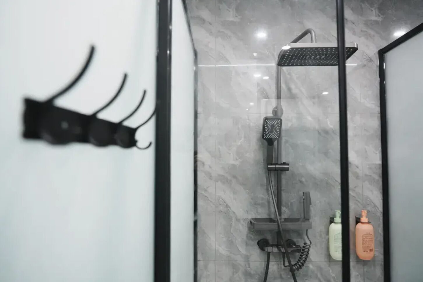 Uma casa de banho moderna com cabine de duche em vidro, toalheiro preto e duas embalagens de produtos de higiene pessoal.