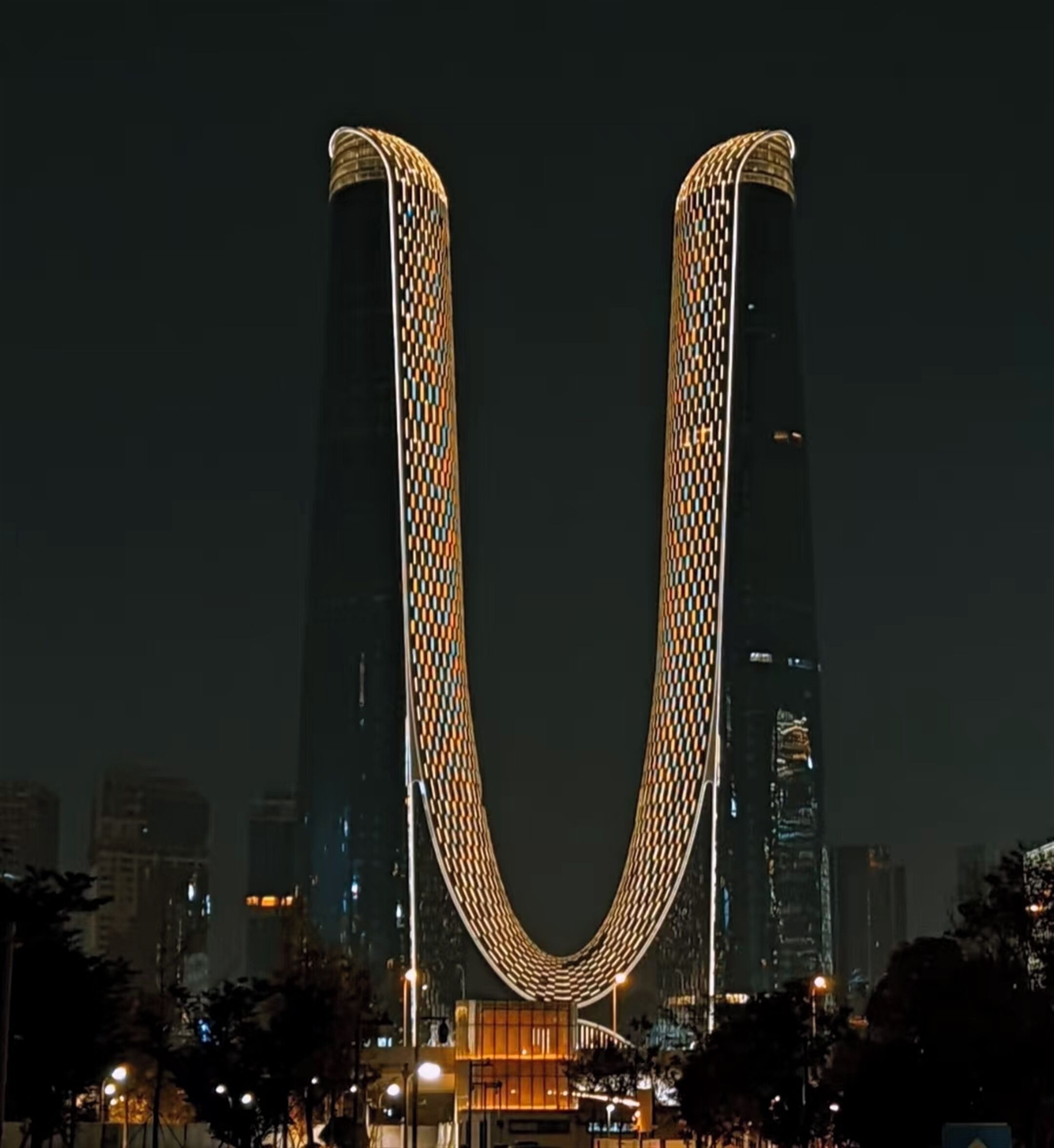 A nighttime view of a cityscape with a prominent building featuring a distinctive U-shaped structure.