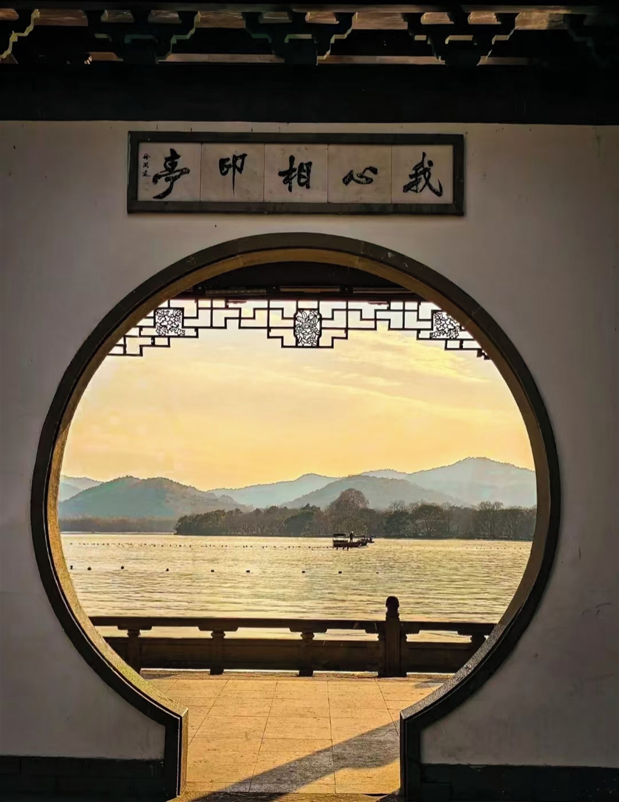 Una finestra circolare con vista su un lago, montagne e una barca.