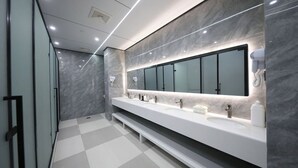 Un baño moderno con un espejo grande, varios lavamanos y un secador de pelo en la pared.