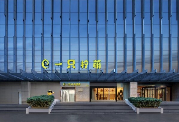 Hotel entrance with glass door and well-maintained hedges.