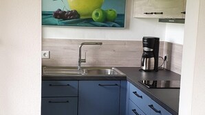 A kitchen with blue cabinets, a stainless steel sink, and a coffee maker. - Ferienwohnung Nr. 23, 55 qm, 2 Personen, 1 Schlafzimmer, Balkon (Unterwössen)