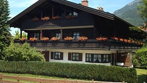 A two-story building with a dark facade, multiple windows, and a balcony with flowers. - Ferienwohnung Nr. 23, 55 qm, 2 Personen, 1 Schlafzimmer, Balkon (Unterwössen)